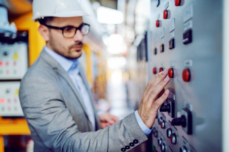 Man in a gray suit and helmet operates machinery controls in an industrial setting.