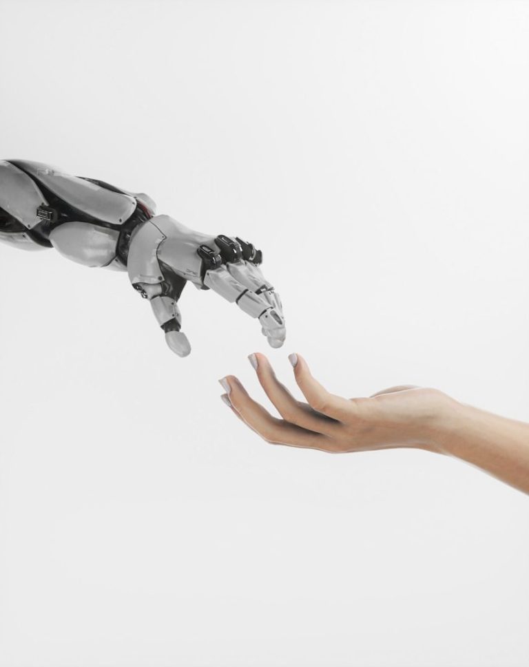 A robotic hand reaching toward a human hand against a plain background.