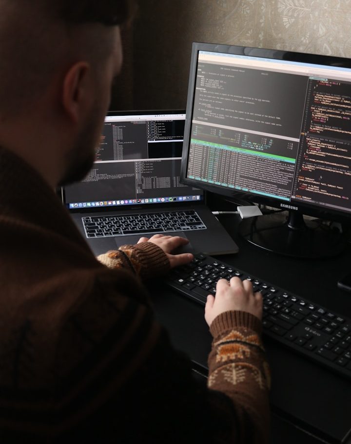Person coding at a desk with multiple computer screens displaying code.